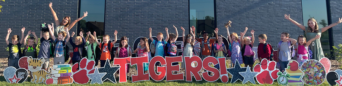 Students and staff with arms reaching out behind a sign that reads Tigers!