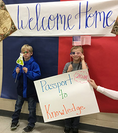 Students with signs saying Passport to Knowledge and Welcome Home